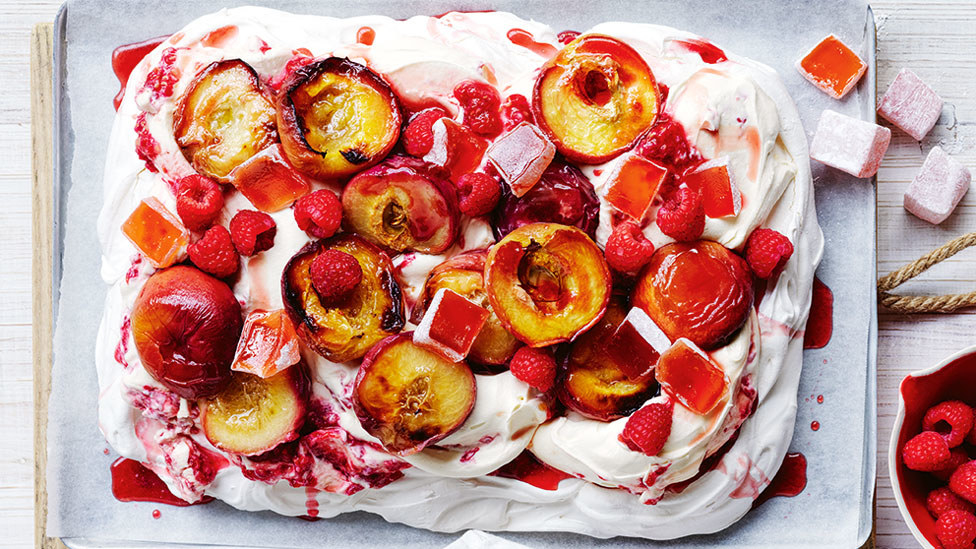 Square pavlova topped with heavy cream, peach halves, raspberry and Turkish delight jellies