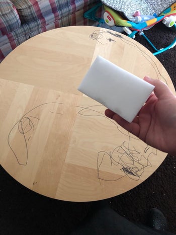 Reviewer holding eraser sponge in front of wood table with permanent marker markings