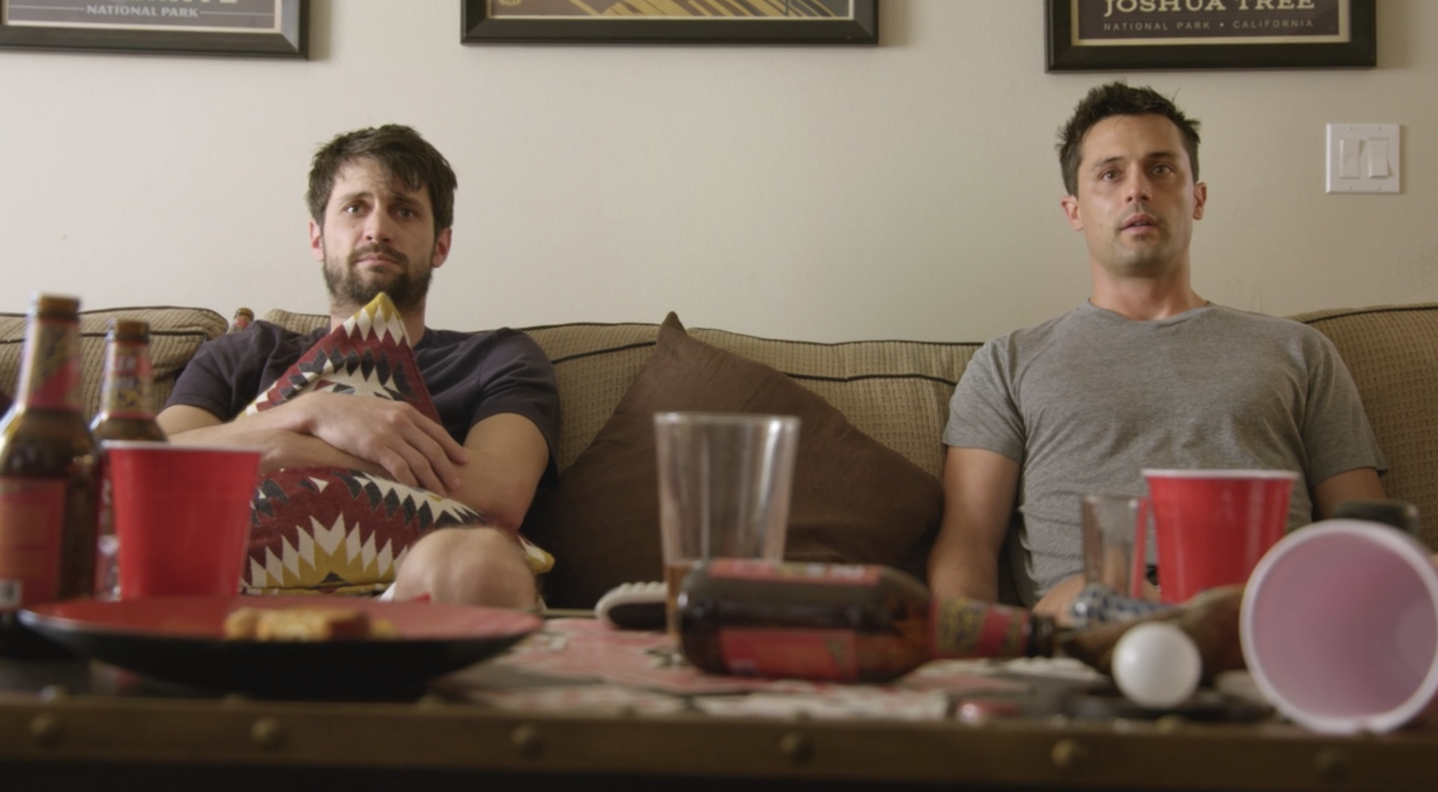 James Lafferty and Stephen Colletti sitting on a couch behind a table strewn with Solo cups and beer bottles