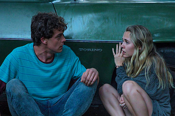 Caleb (Israel Broussard) and Rain (Madison Iseman) crouching down on the ground while leaning against the side of a car