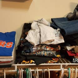 Messy T-shirt piles above a closet rod