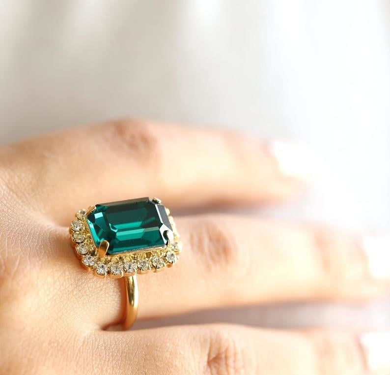 Hand wearing gold ring with small crystals and large emerald center stone