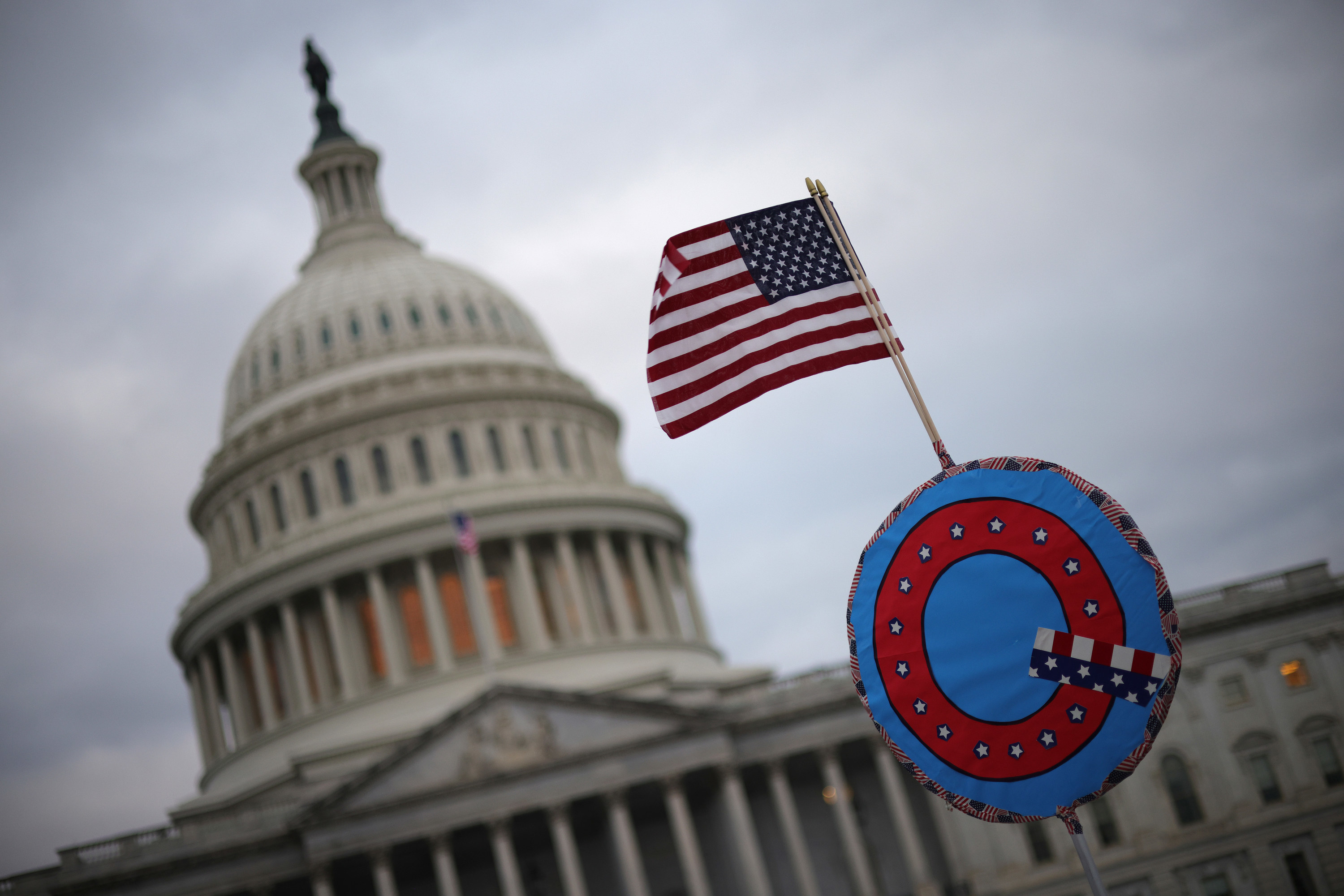 A mini US flag set atop a &quot;Q&quot; in front of the Capitol