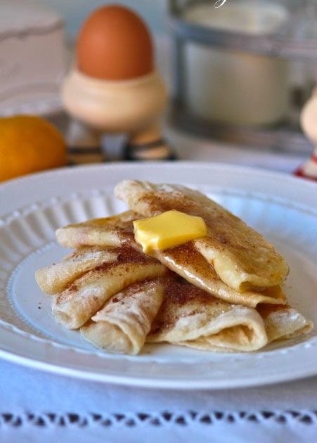 Several potato pancakes rolled up topped with cinnamon sugar and butter.