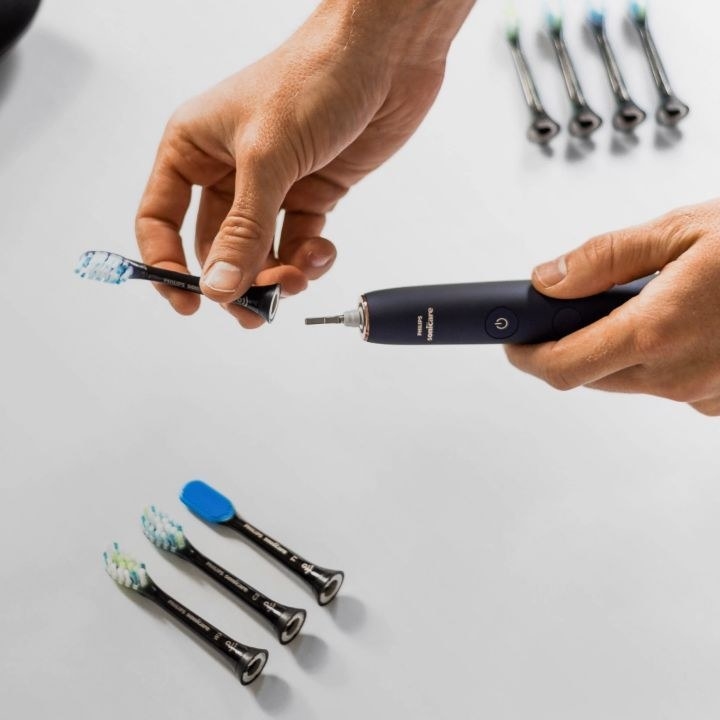 A person swapping out the brush head with three others on a counter 