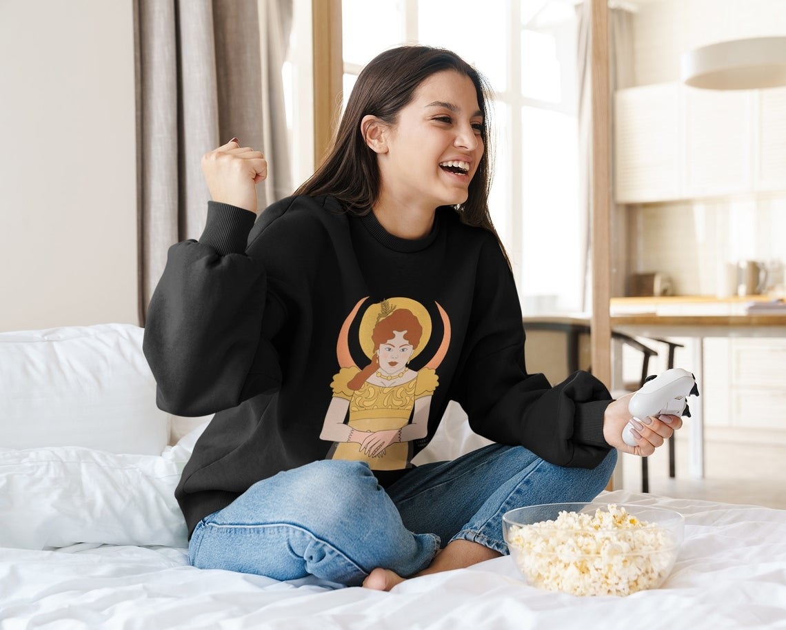 A person wearing the sweatshirt while eating popcorn and holding a gaming remote