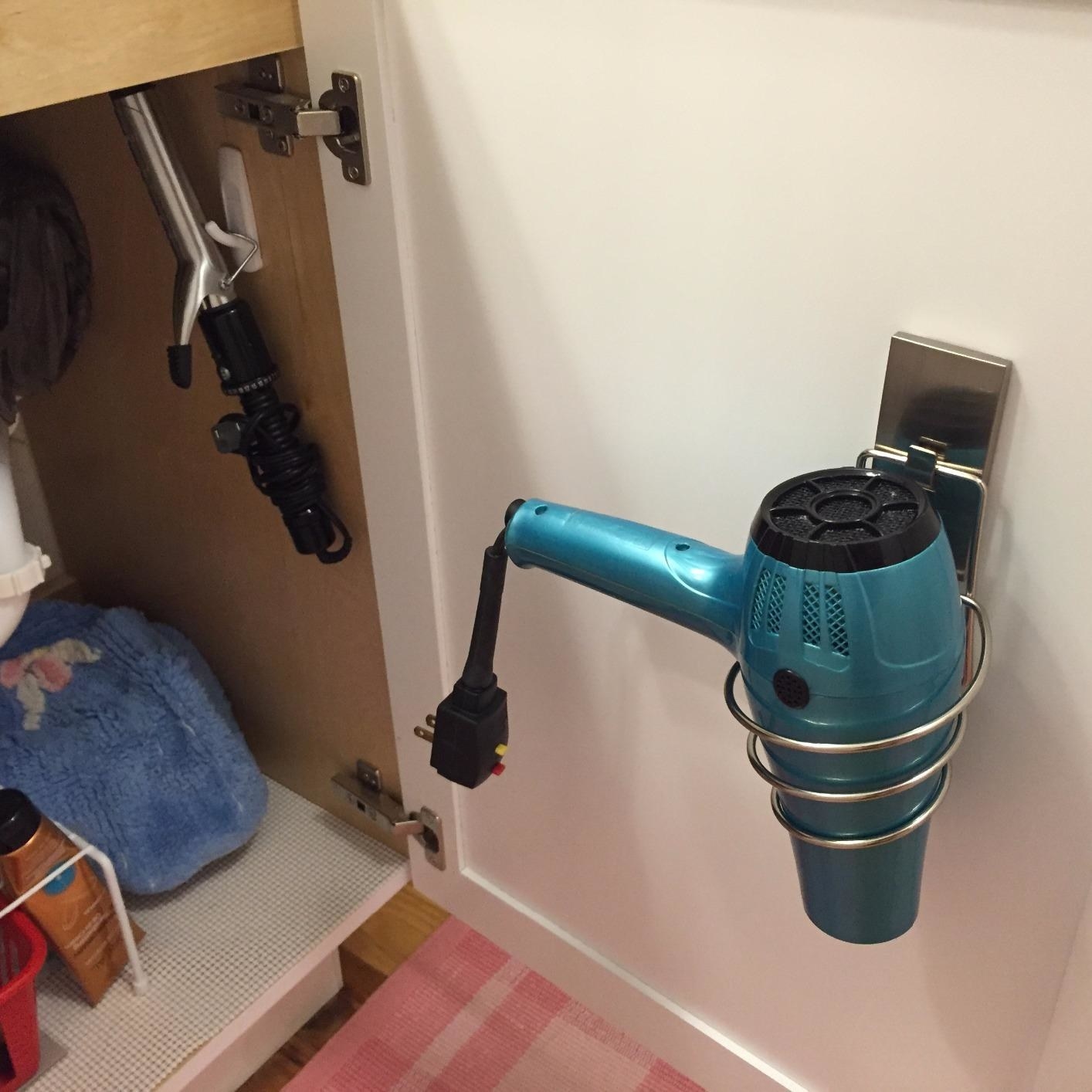 inside of reviewer&#x27;s bathroom cabinet door, hairdryer sits nose-down in spiral metal holder