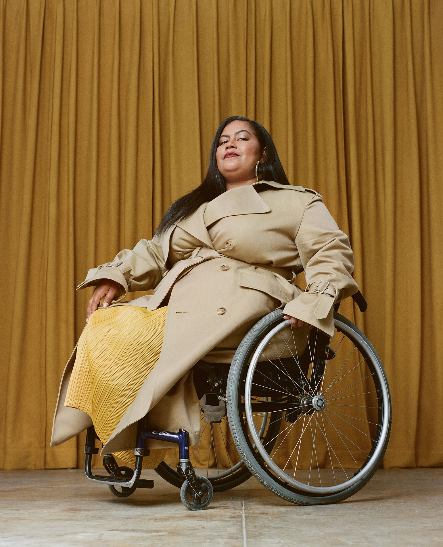 A woman in a trenchcoat and a wheelchair poses for a portrait