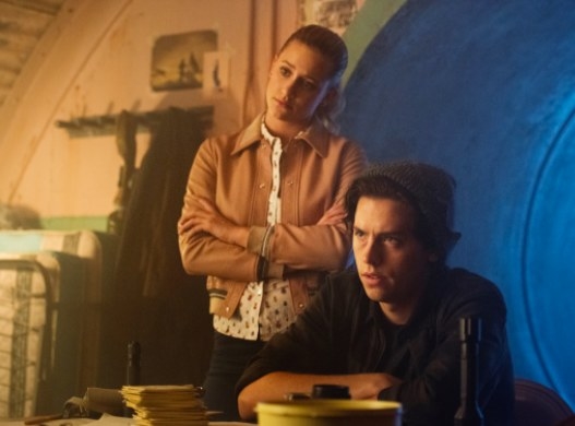 Betty stands behind Jughead in a bunker; they both have their arms crossed