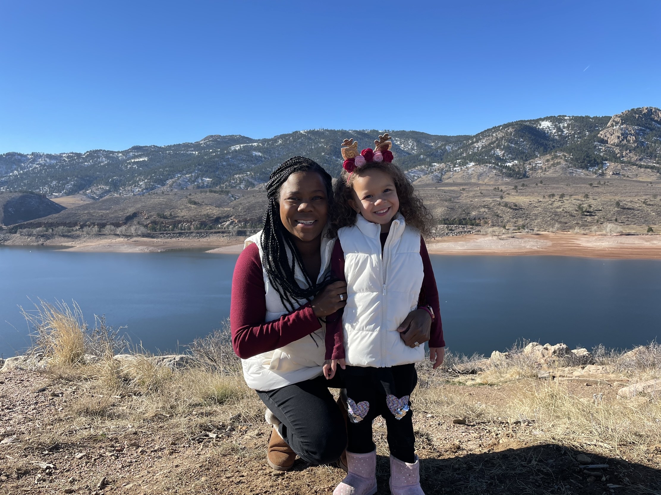 Melissa Burt poses with her young daughter in front of mountains and a lake