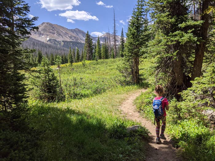Emily Fischer's young child is on the side of a lush hiking trail, with mountains in the distance