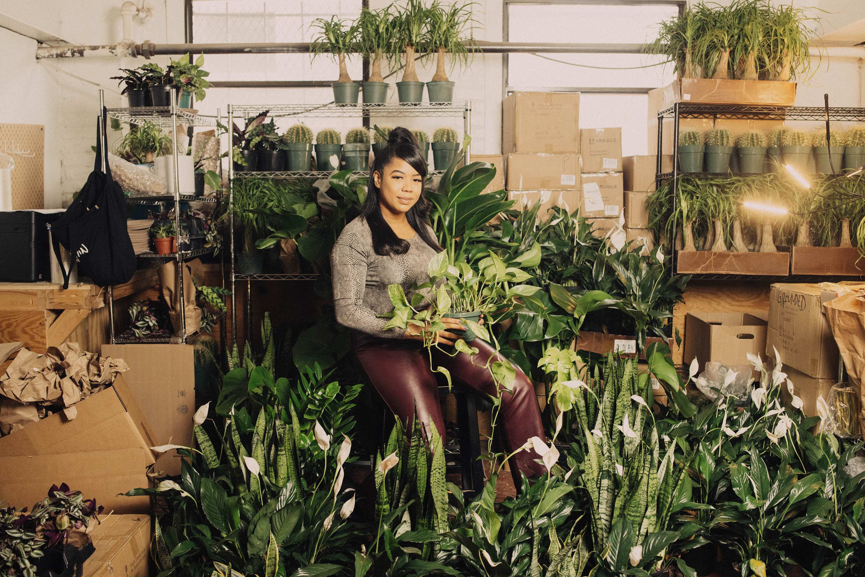 A woman sitting among many plants in a store she owns