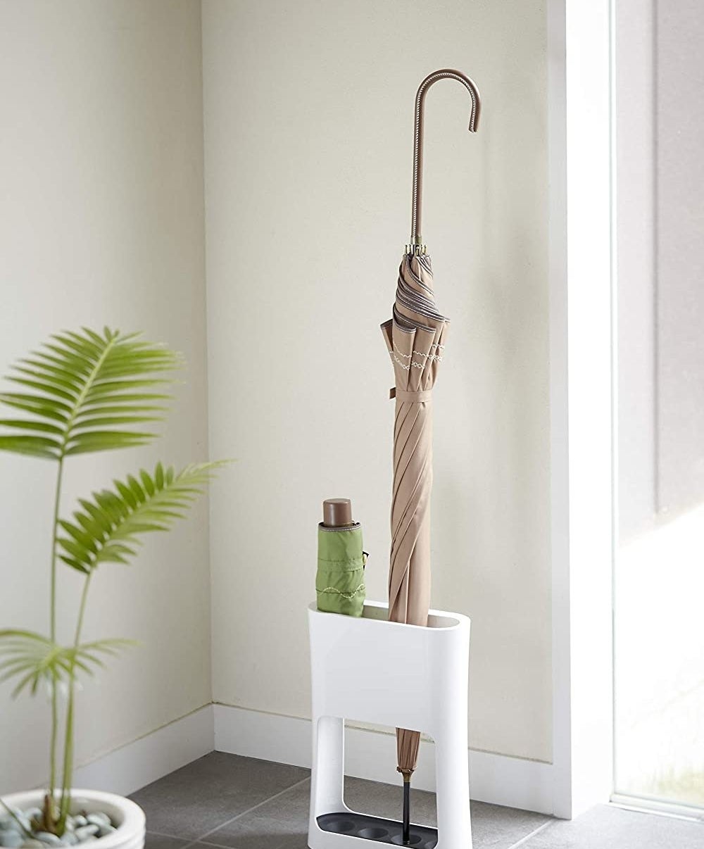 The umbrella stand with a large umbrella and a small portable one sitting inside 