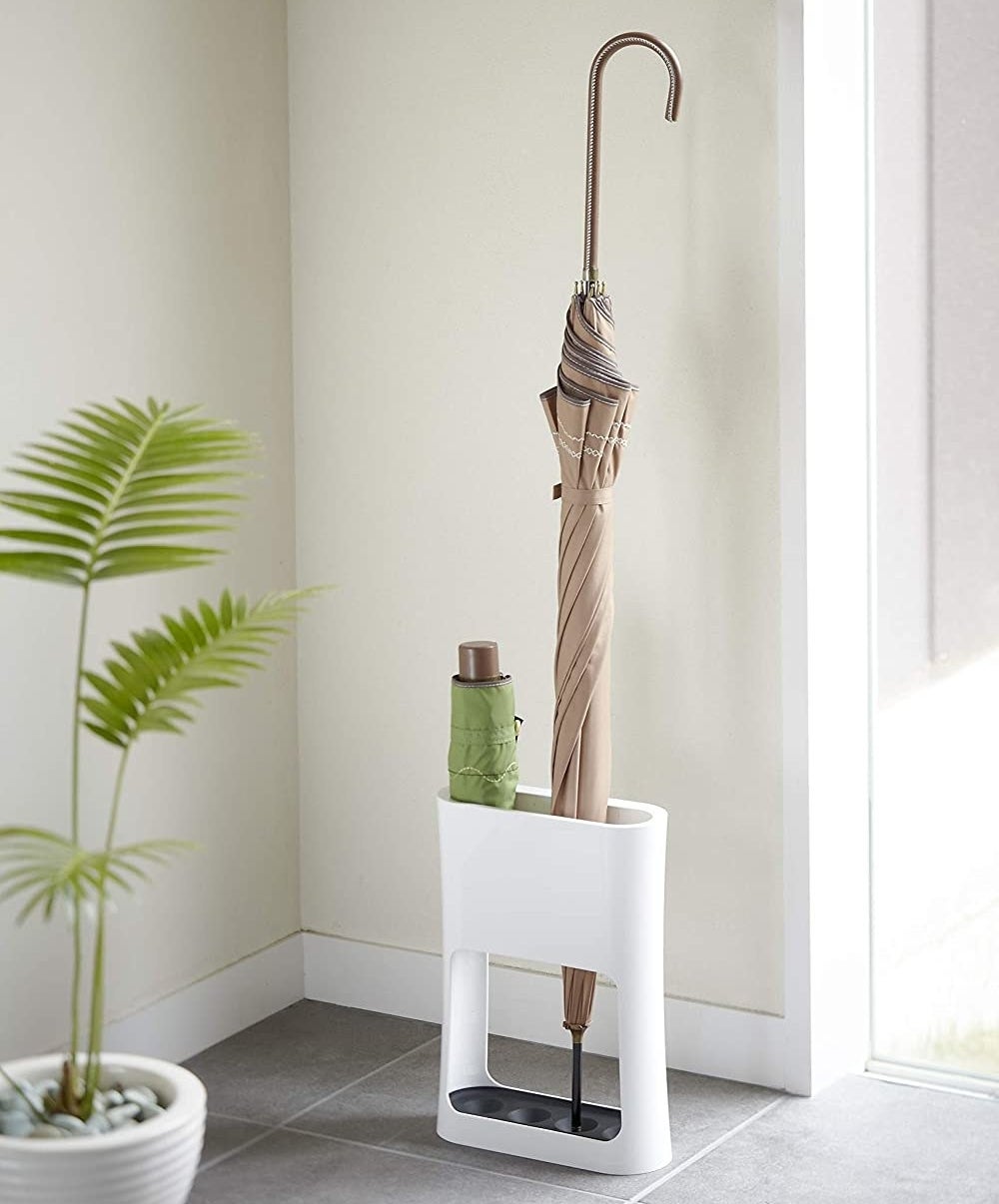 The umbrella stand with a large umbrella and a small portable one sitting inside