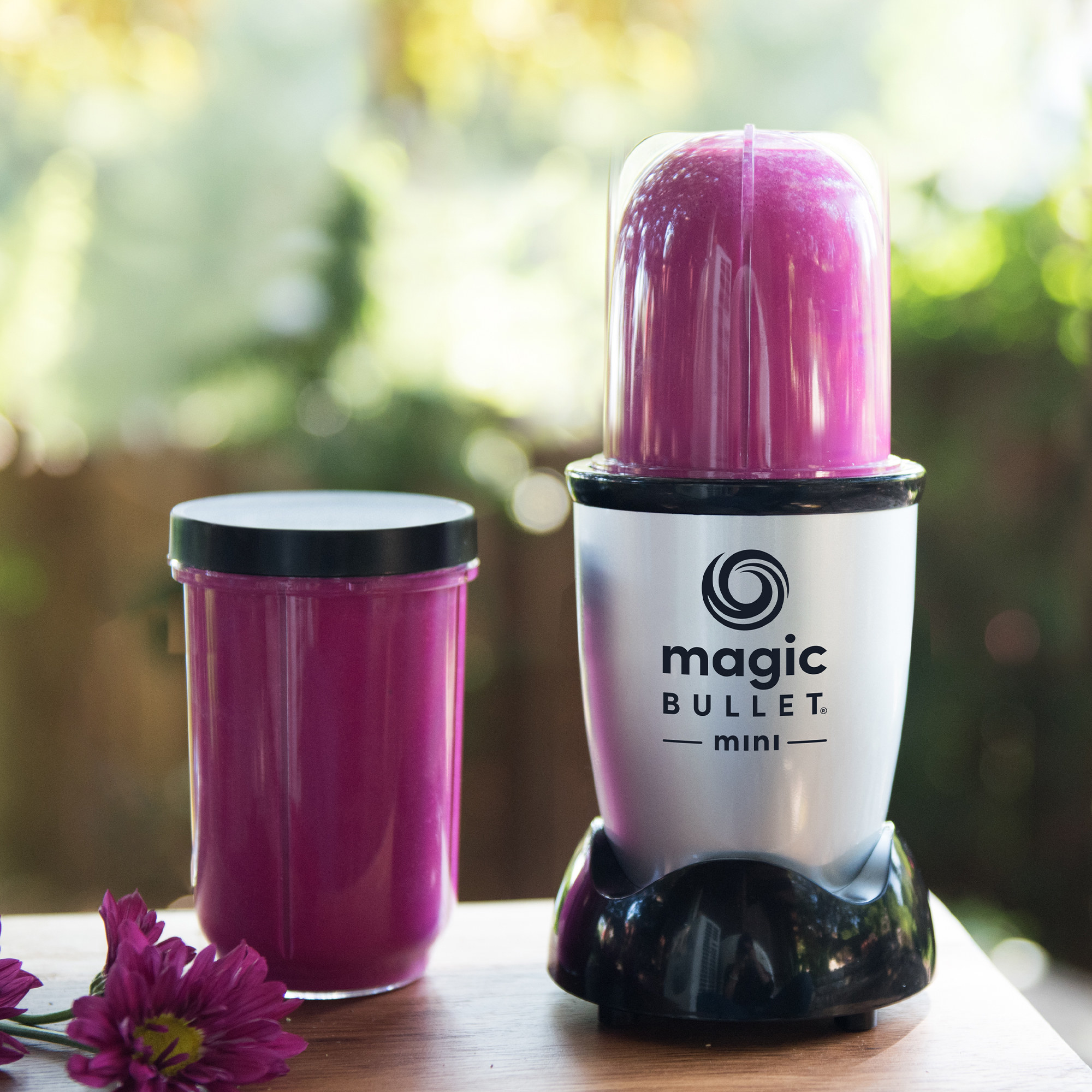 A silver blender with a black base and clear plastic cup filled with a fuchsia-colored smoothie