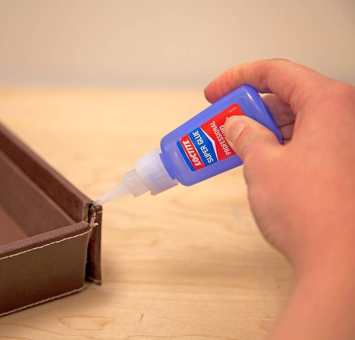 person using super glue to repair a tear in a brown leather item