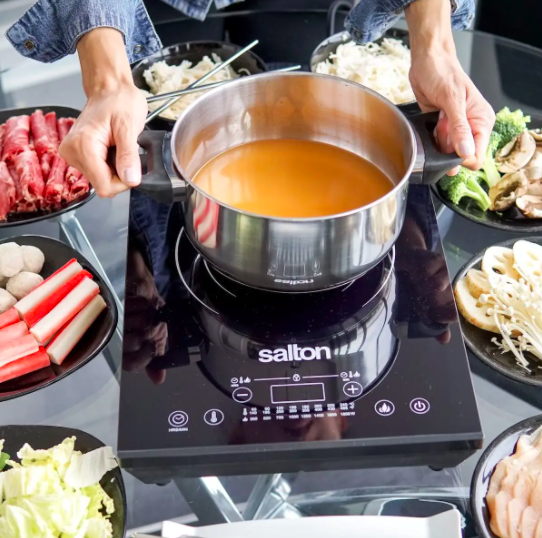 A person placing a pot of soup onto the induction cooktop