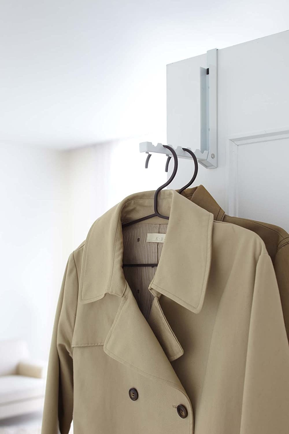 A folding hook on a door frame holding several coats on clothes hangers