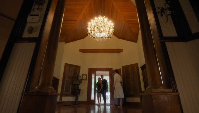 Two people standing in the doorway of a home with tall ceilings and a chandelier. 