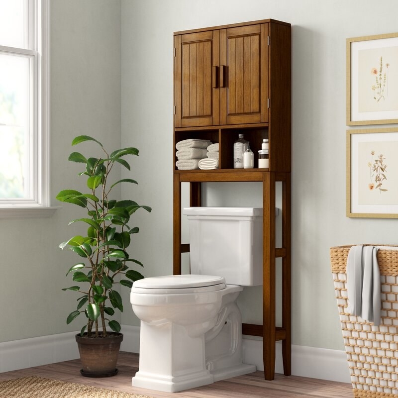 a brown wood over the toilet storage system with two cubbies and doors