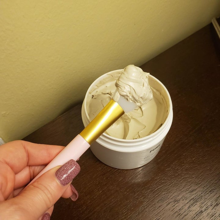 Reviewer holds same face mask applicator in hand over jar filled with white face mask cream