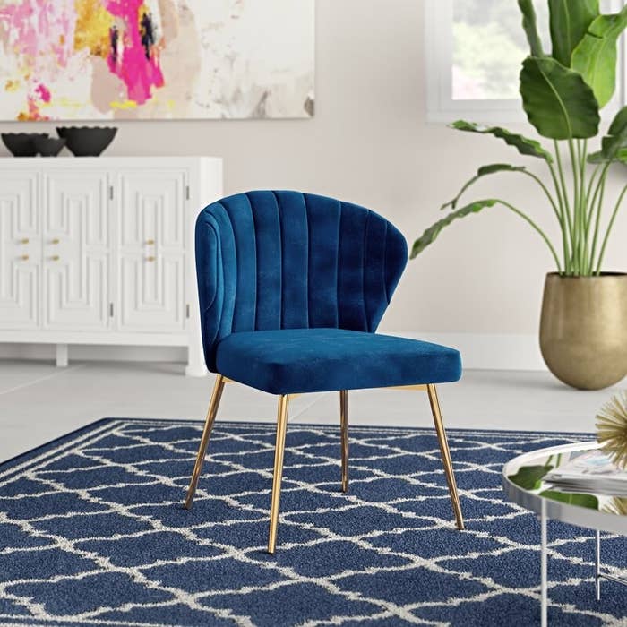 a blue velvet tuft chair with gold legs in a room