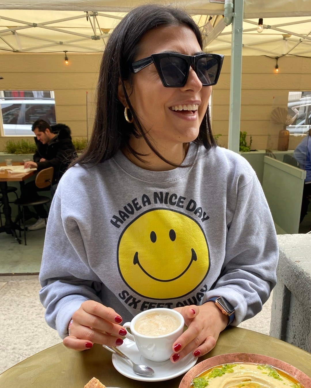 buzzfeed employee wearing a gray sweatshirt with a yellow smiley on it and the words &quot;have a nice day six feet away&quot; on it