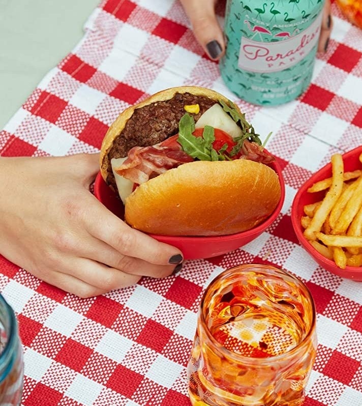 a hand holding a burger in the red bowl 