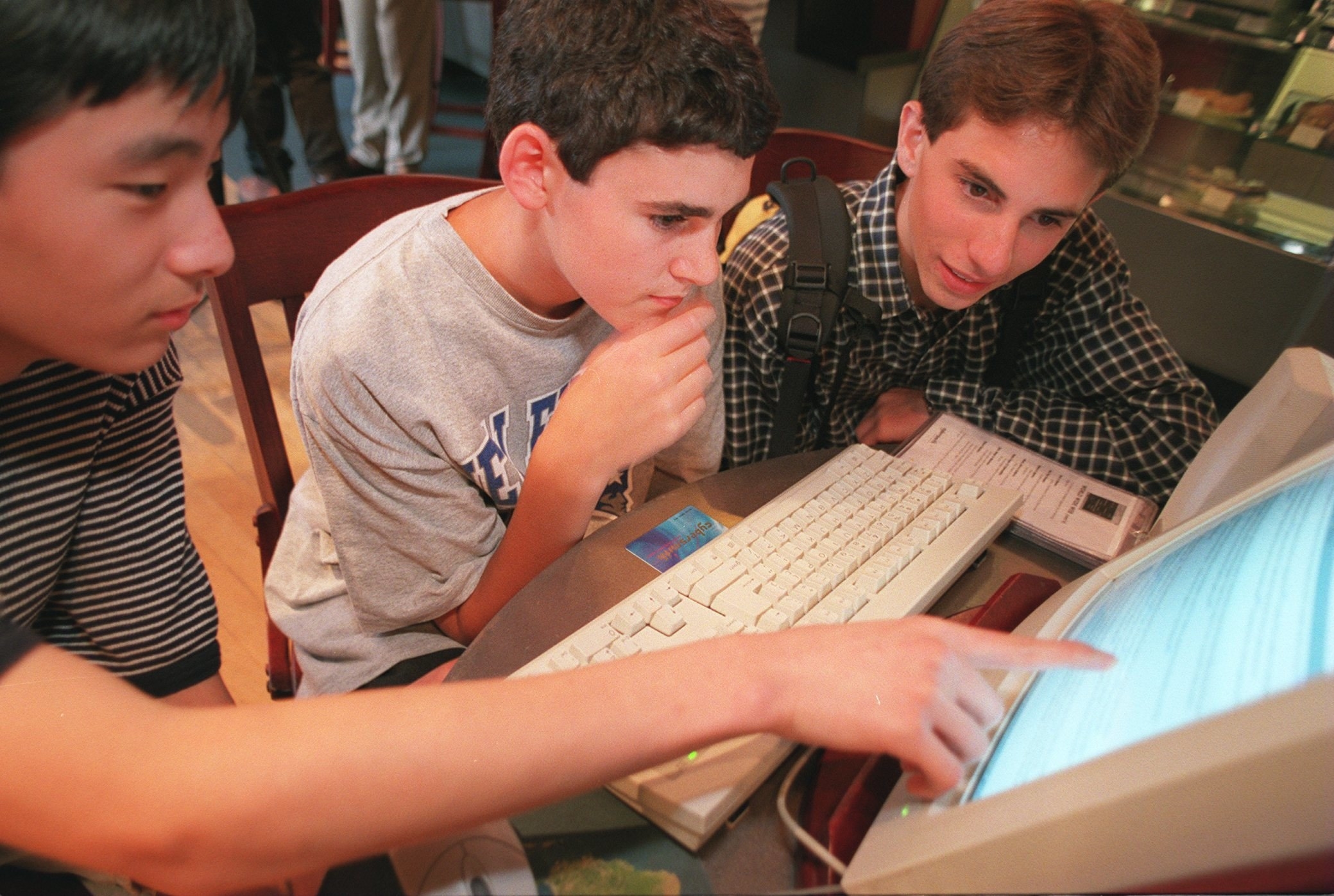 Three teens sitting in front of a desktop computer