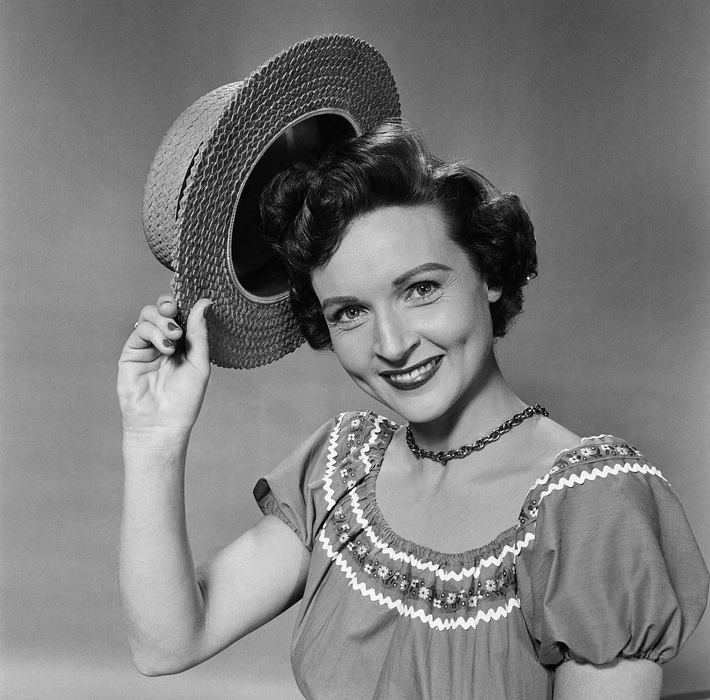 Betty posing for a photo by smiling and tipping her hat