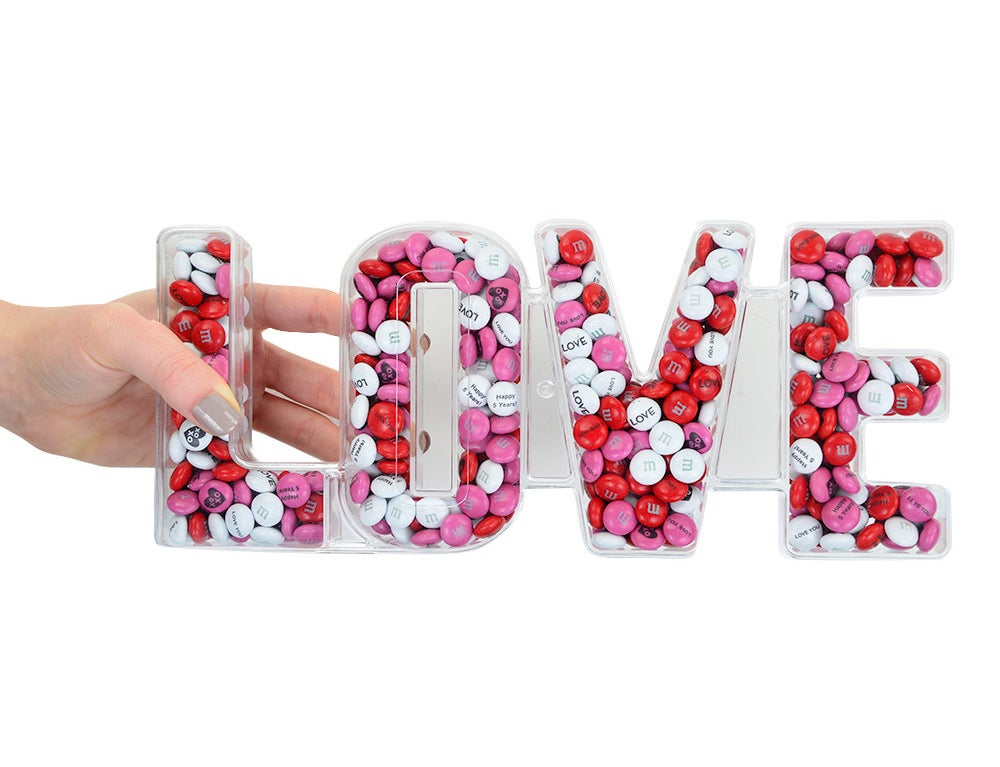 red and white m and ms in a clear box that spells out love