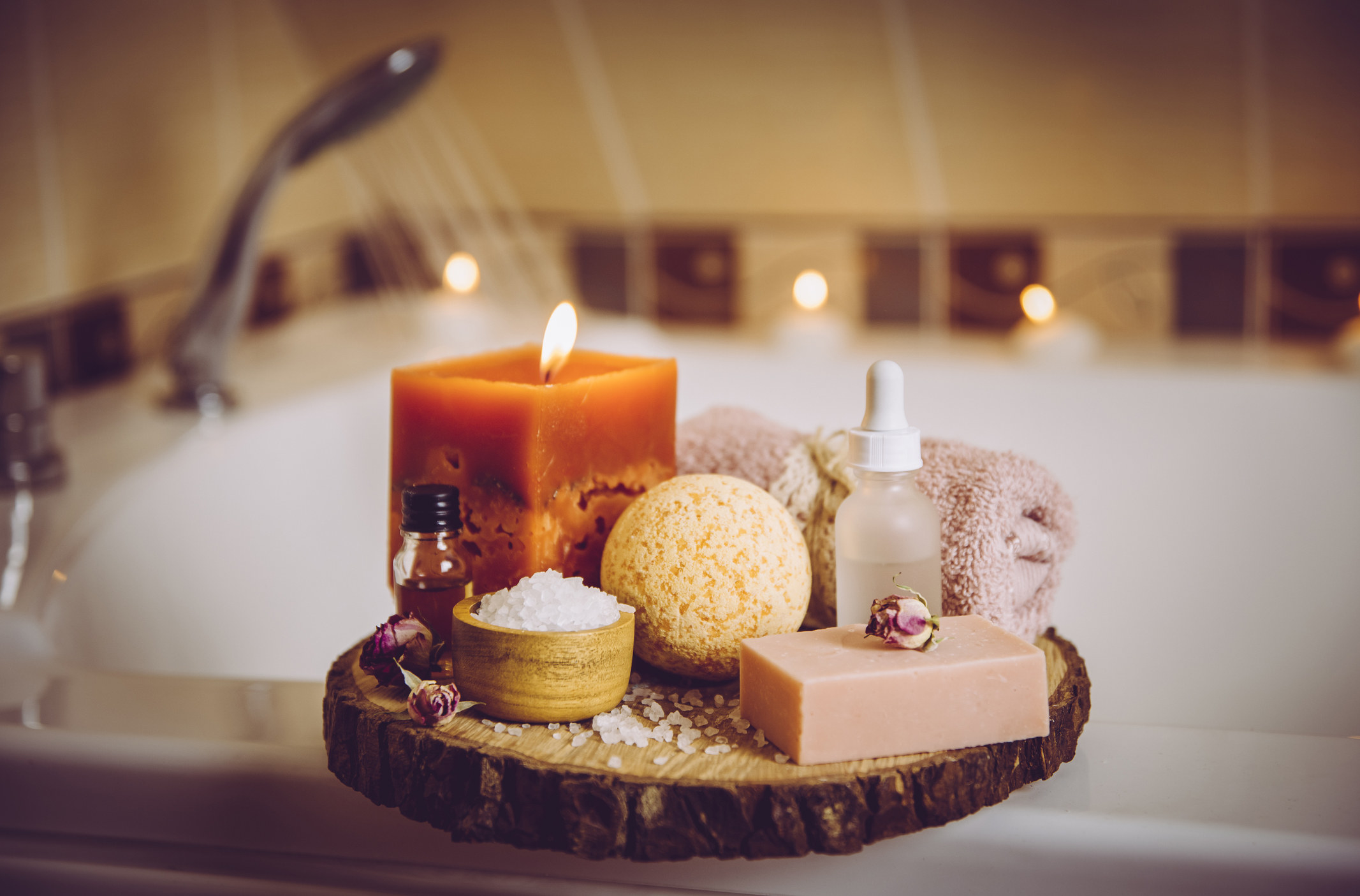 Image of a bath with a candle, essential oils, and bath salts on the side of the tub.