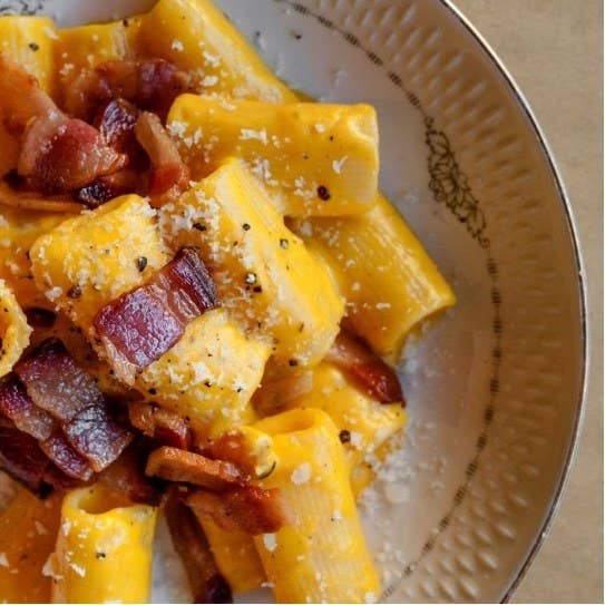close up of a plate of rigatoni with pecorino cheese and guanciale on top