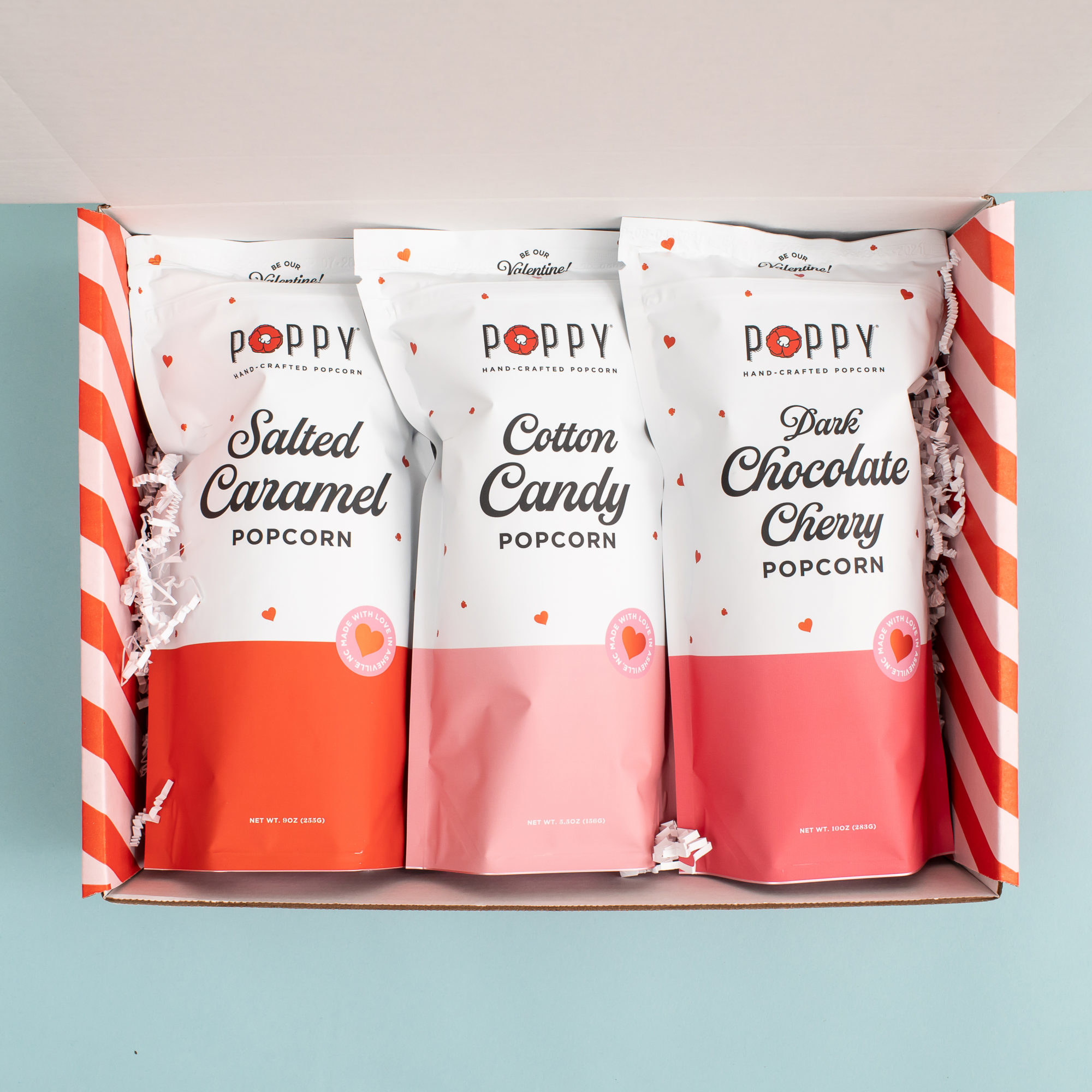 three bags of popcorn with pink and red packaging in a box with red and pink stripes