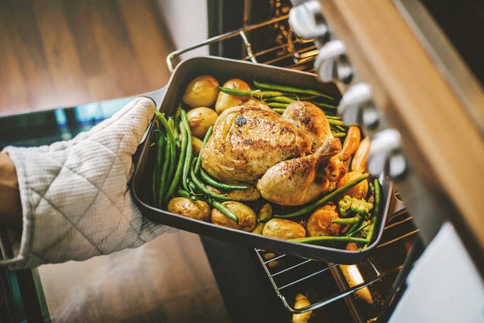 Cook taking ready fried baked chicken with vegetables from the oven