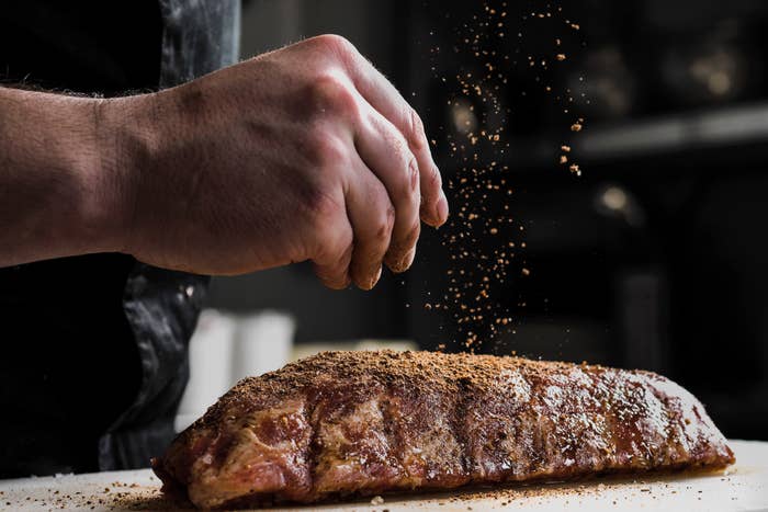 The hand of a male chef putting salt and spices on meat