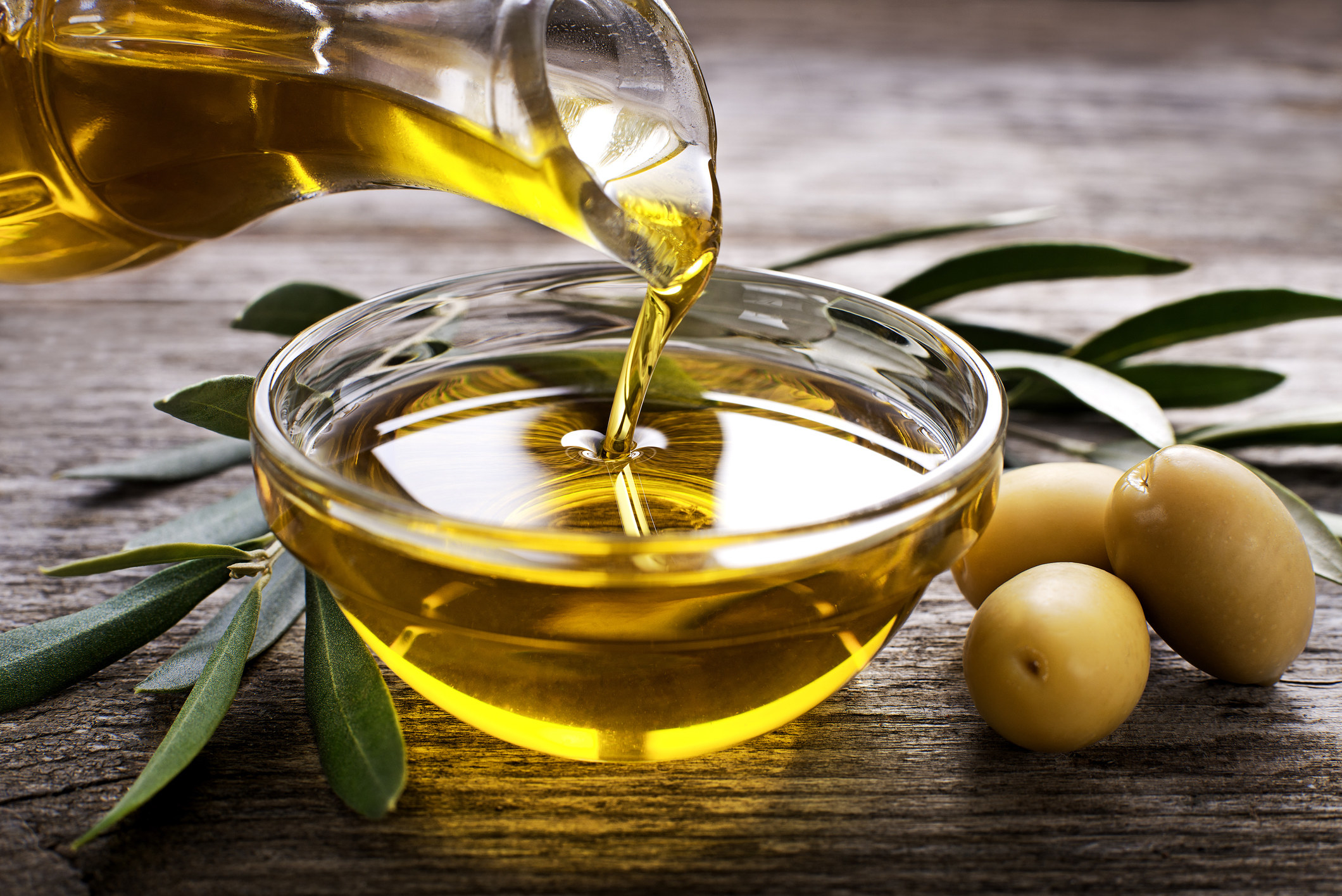 Close-up of olive oil being poured into a clear glass bowl