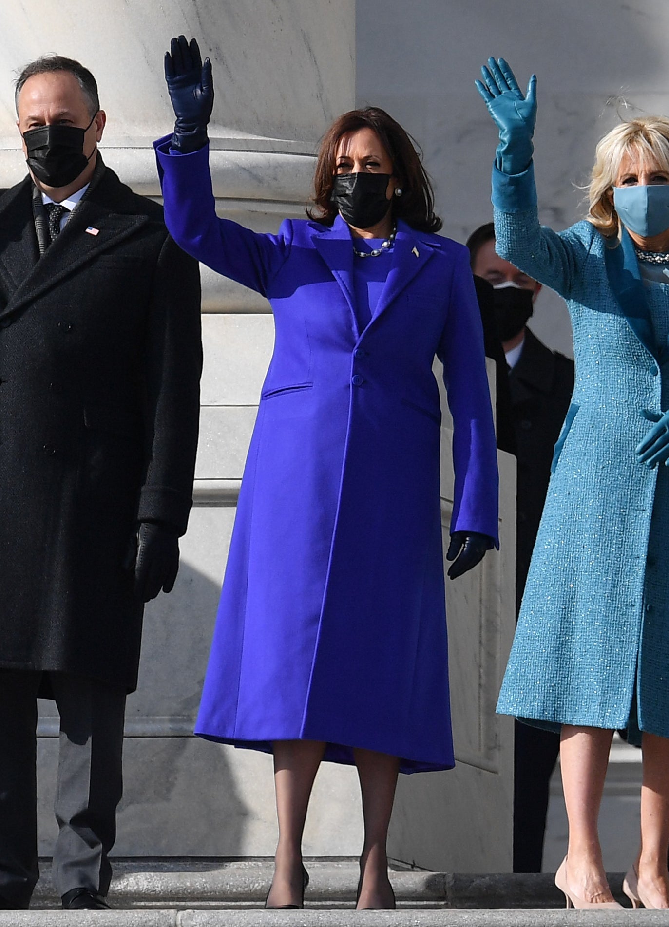 Kamala Harris is a long, deep blue coat with matching shirt, dark blue leather gloves, and black facemask.