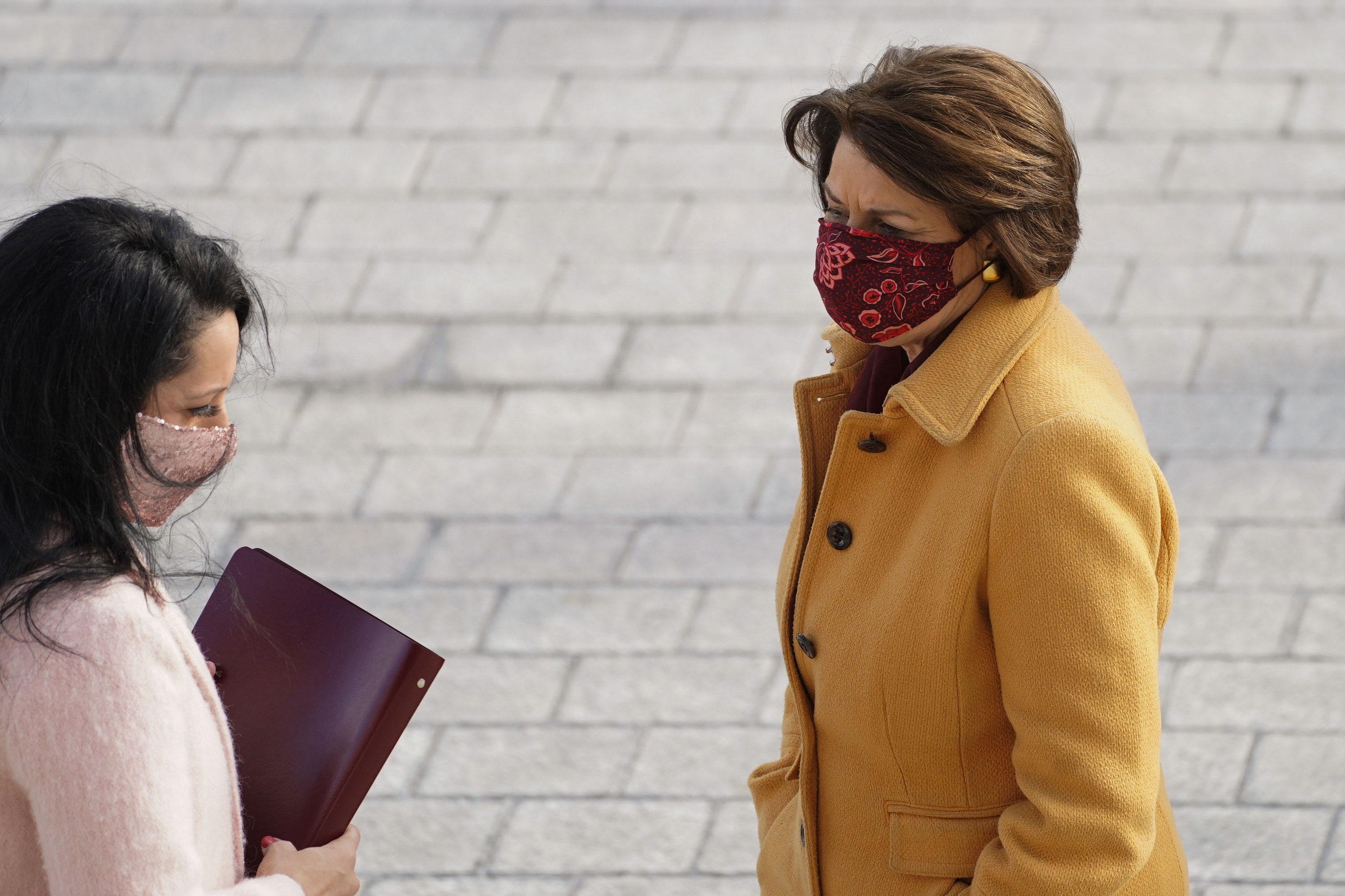 Sen. Amy Klobuchar in a yellow coat and red floral face mask at the inauguration, standing next to a woman in a pink coat and pink face mask. 