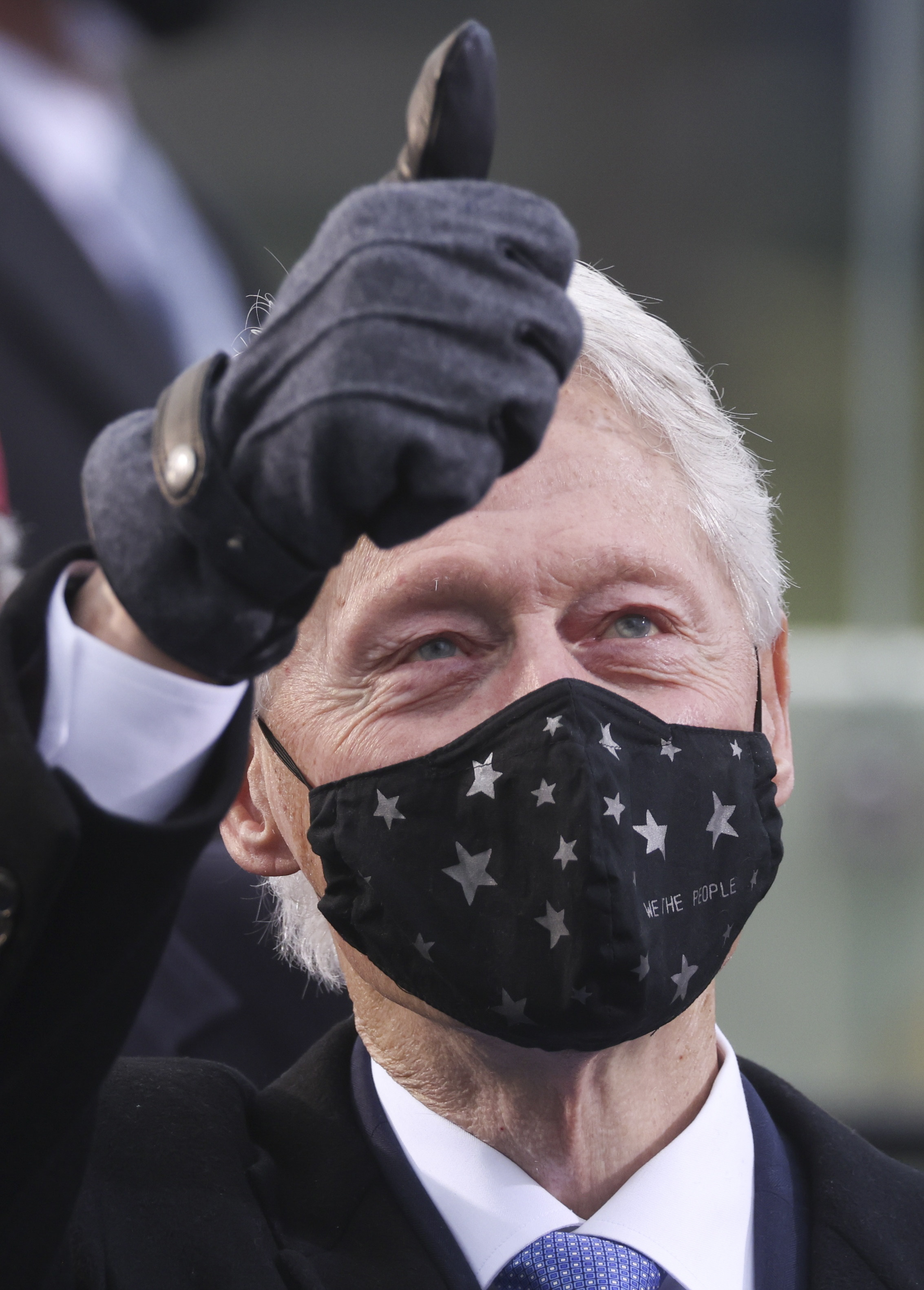 Bill Clinton wearing a black face mask with stars and giving a thumbs up at the inaguration.