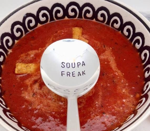 A soup spoon stamped with &quot;SOUPA FREAK&quot; over a bowl full of red soup 