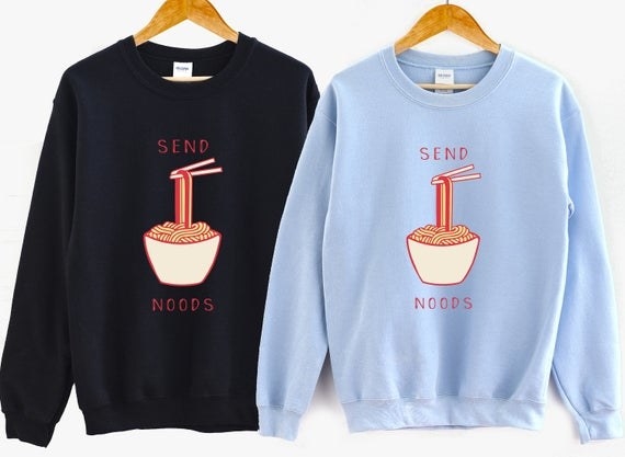A light blue and navy blue crewneck sweatshirt with a screen print of a bowl of ramen noodles that says &quot;Send Noods&quot; 