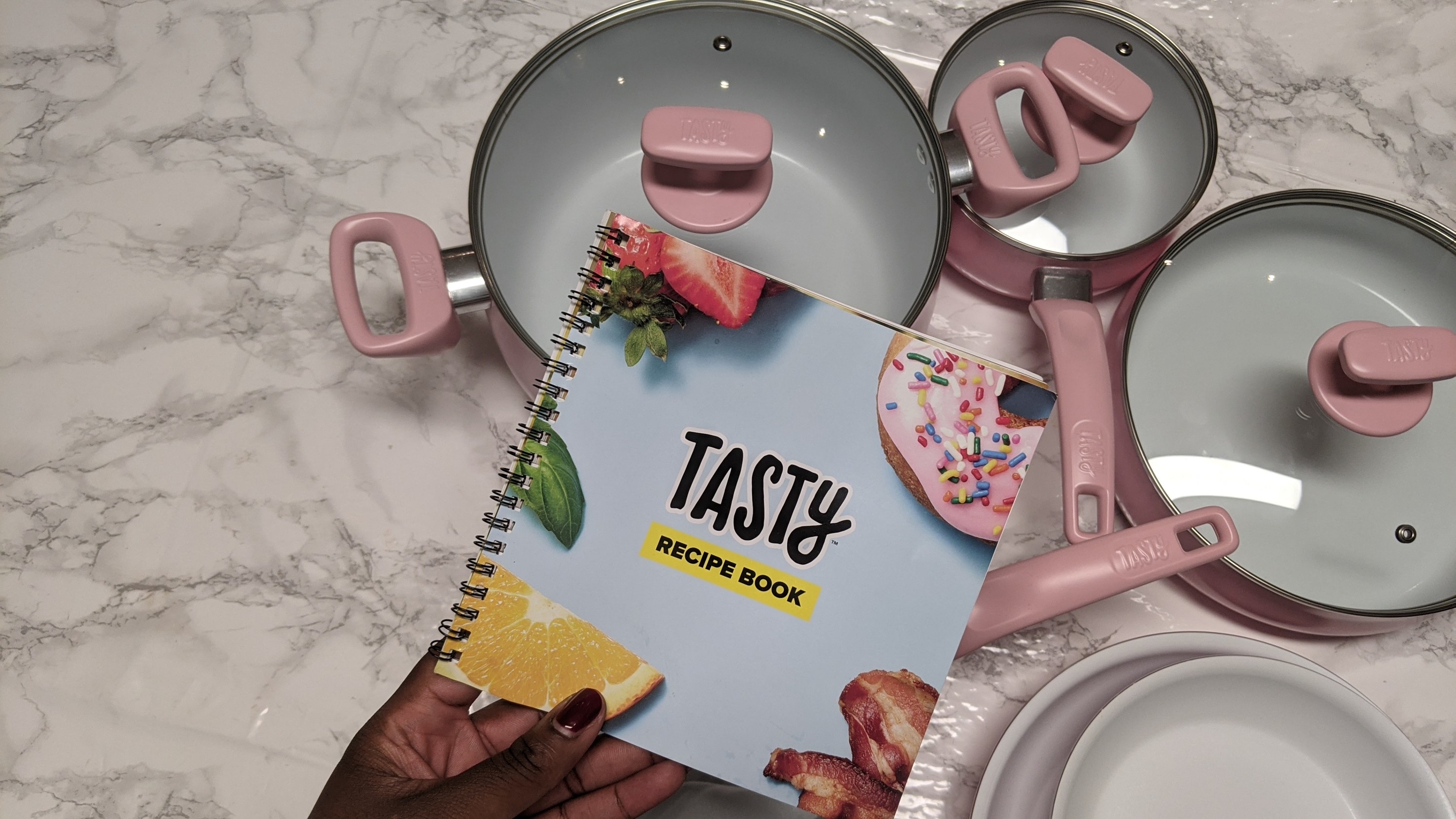 A person holding a recipe book with bunch of pots and pans on the table in front of them