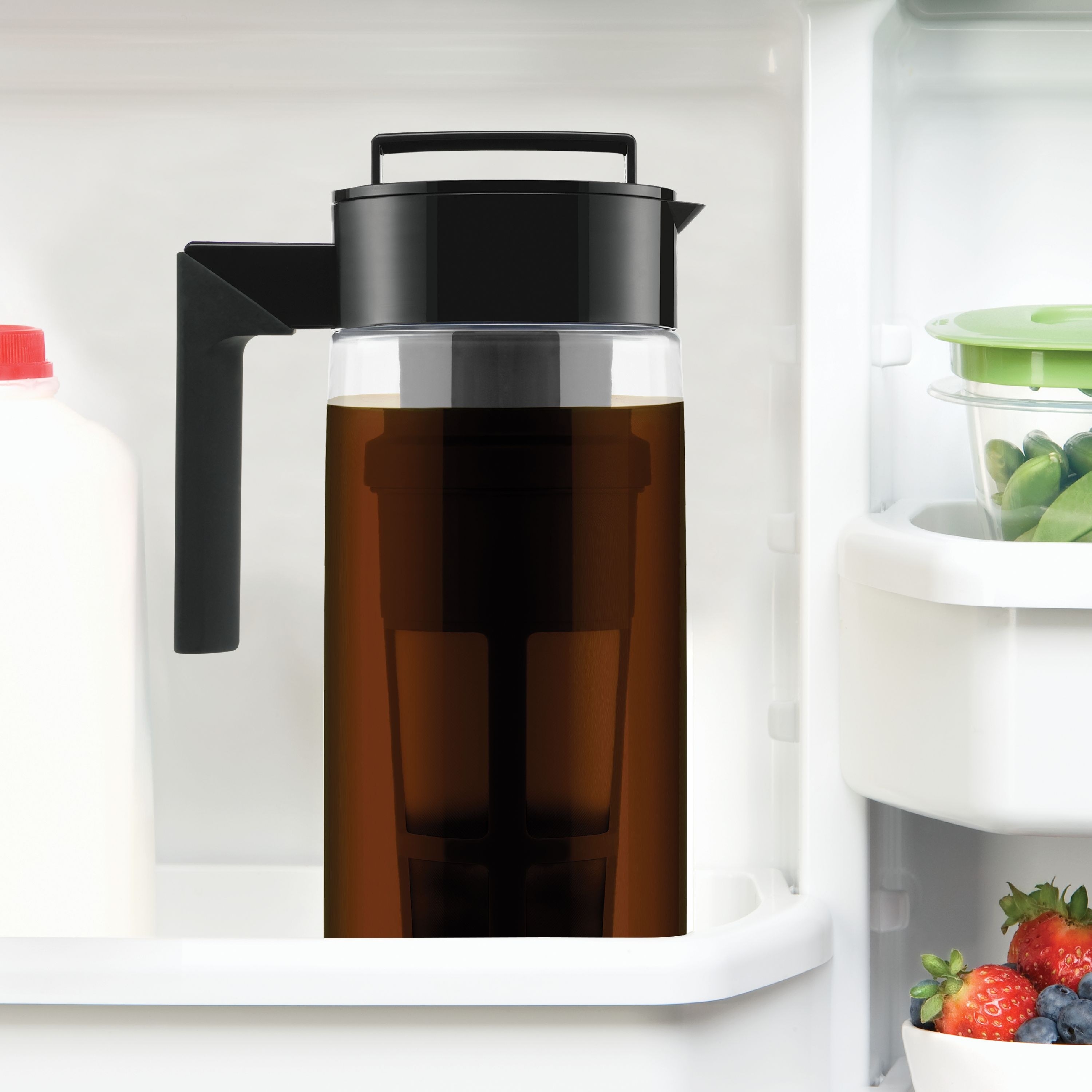 The black and clear cold brew coffee maker filled with coffee on a refrigerator door