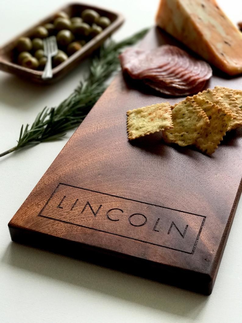 A rectangular wooden cheese board with the name Lincoln carved into it 