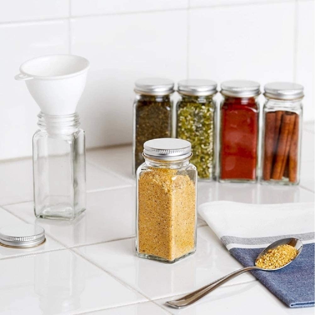 glass bottles filled with spices with one that has a funnel in it