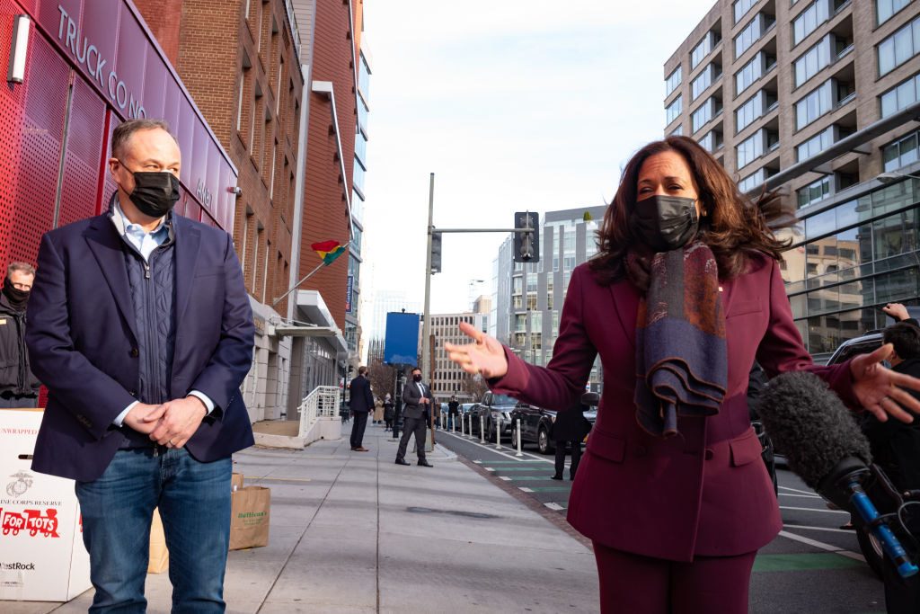 Doug Emhoff standing to the side as Kamala Harris speaks to the press