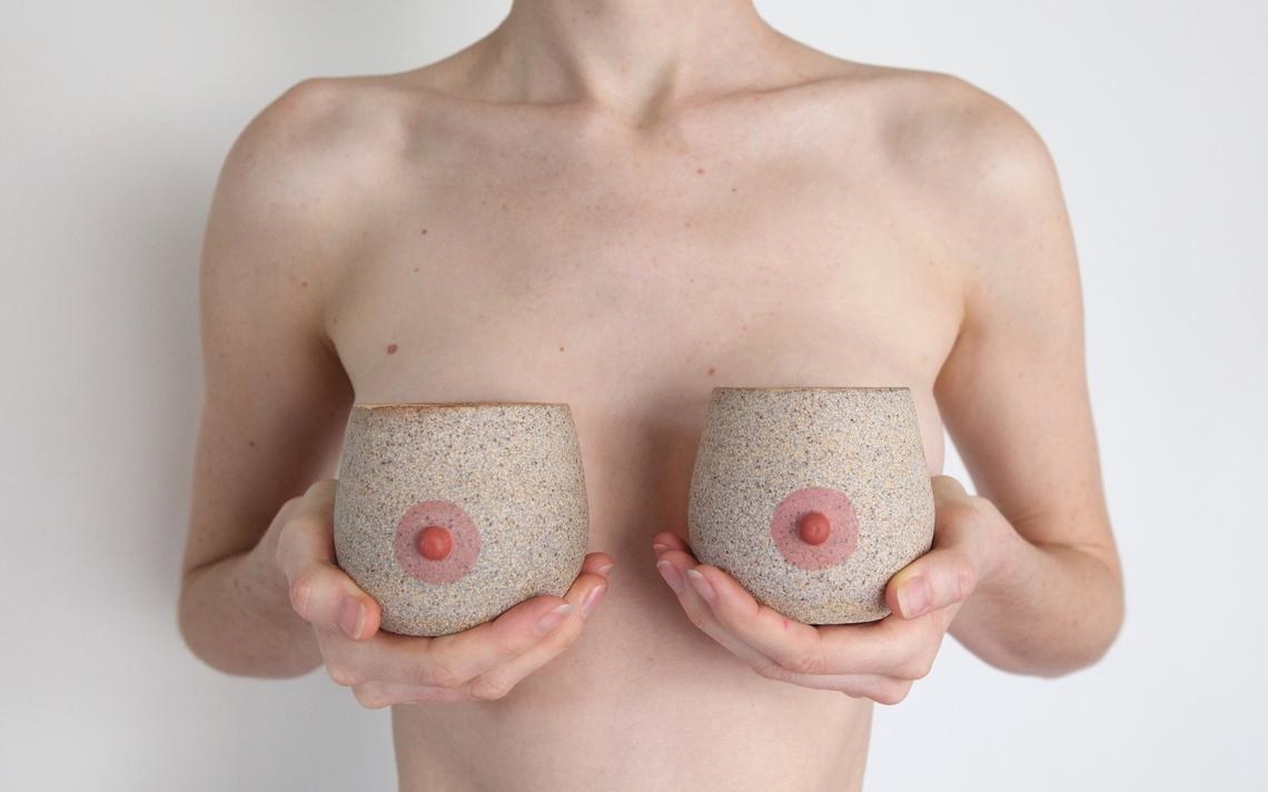 Shirtless person holding boob-shaped mugs in front of chest