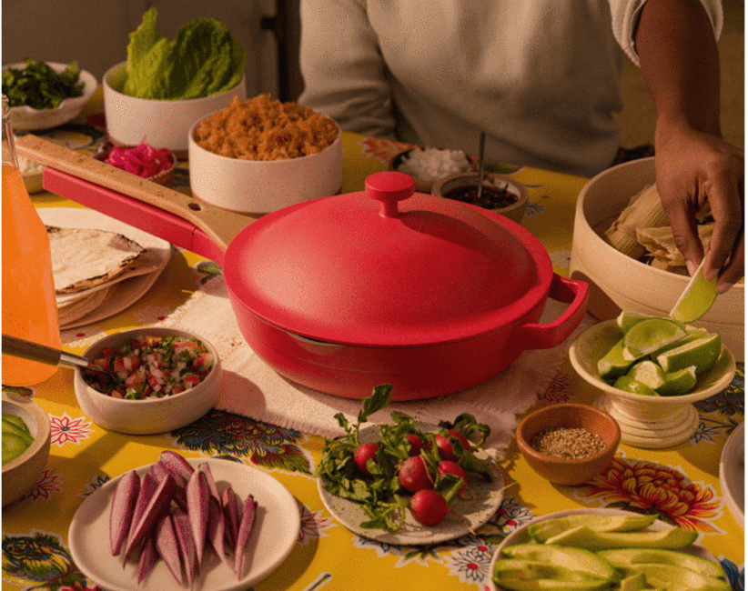 Closeup of the pot and lid in red with the spatula attached to the handle and the lid on top surrounded by food