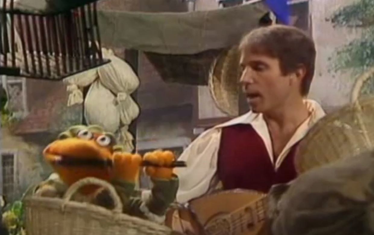 Scooter plays a lute as Paul Simon sings